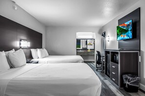 A hotel room with two beds, a desk, a TV, and a bathroom visible through an open door.