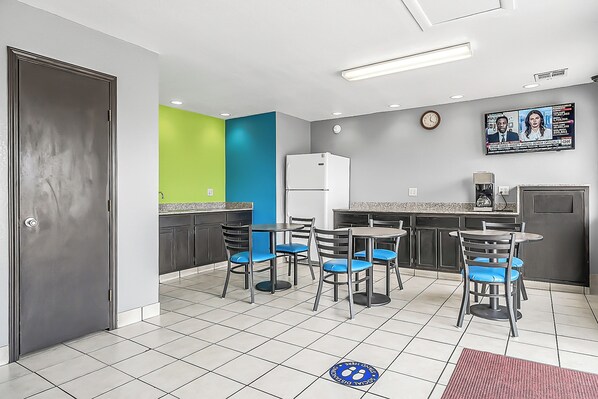 A modern kitchen with a refrigerator, a coffee machine, and a dining area with chairs and a table.