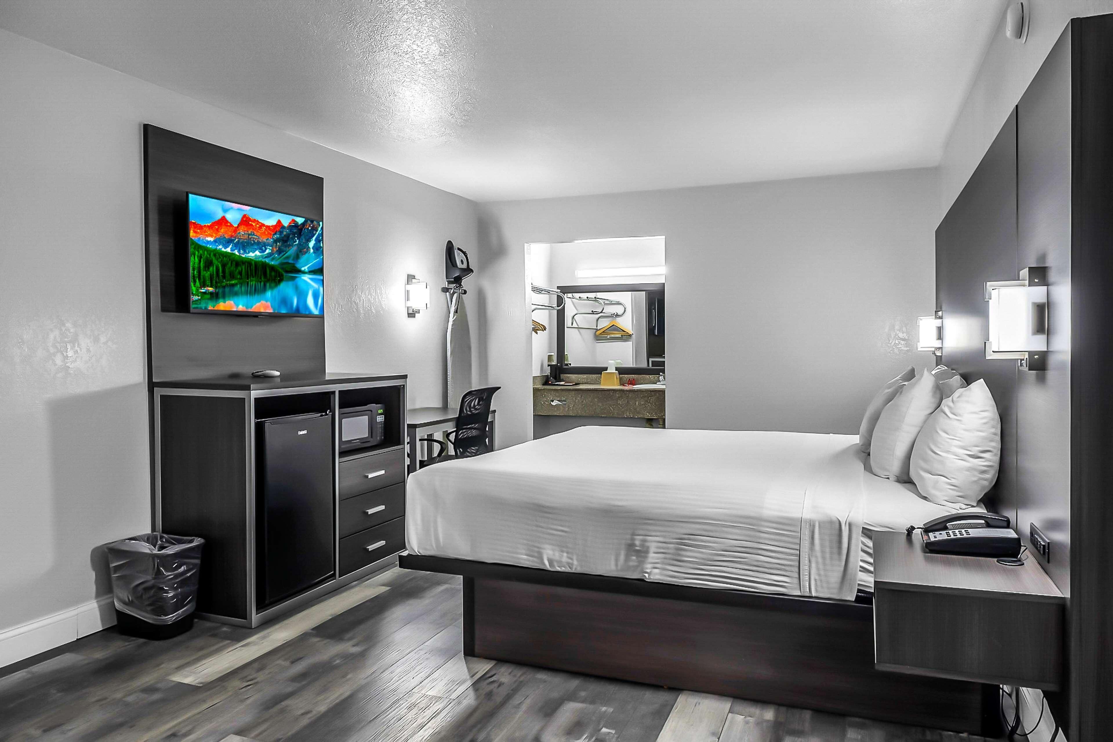 Een moderne hotelkamer met een groot bed, een aan de muur bevestigde televisie, een bureau met een stoel en een kleine prullenbak.