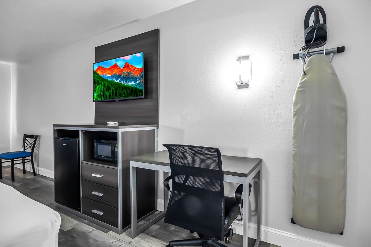 Une chambre d’hôtel équipée d’un téléviseur à écran plat fixé au mur, d’un bureau avec une chaise, d’un four à micro-ondes et d’un mini-réfrigérateur intégré.