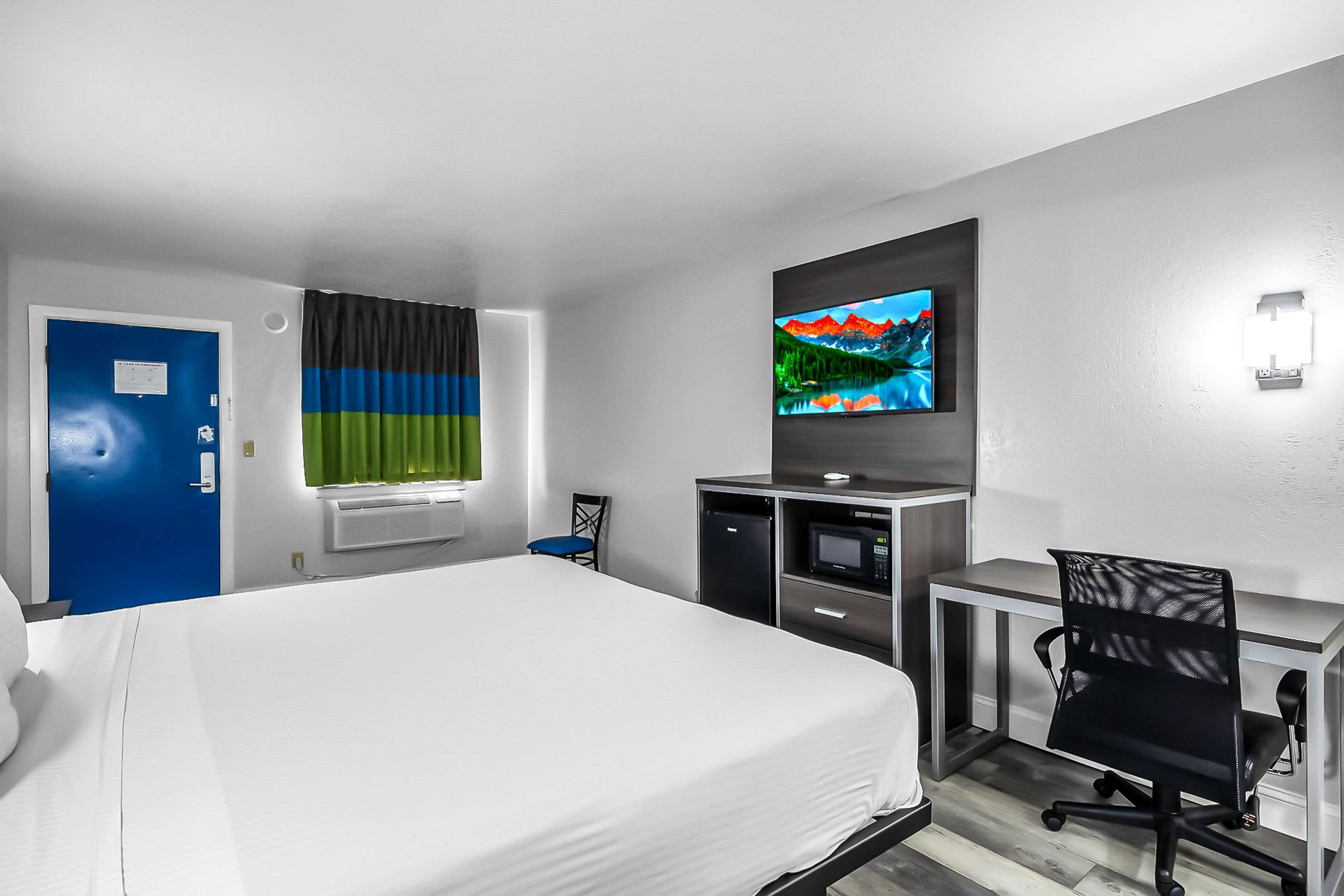 Habitación de hotel con cama, escritorio con computadora, televisión y ventana con cortinas.