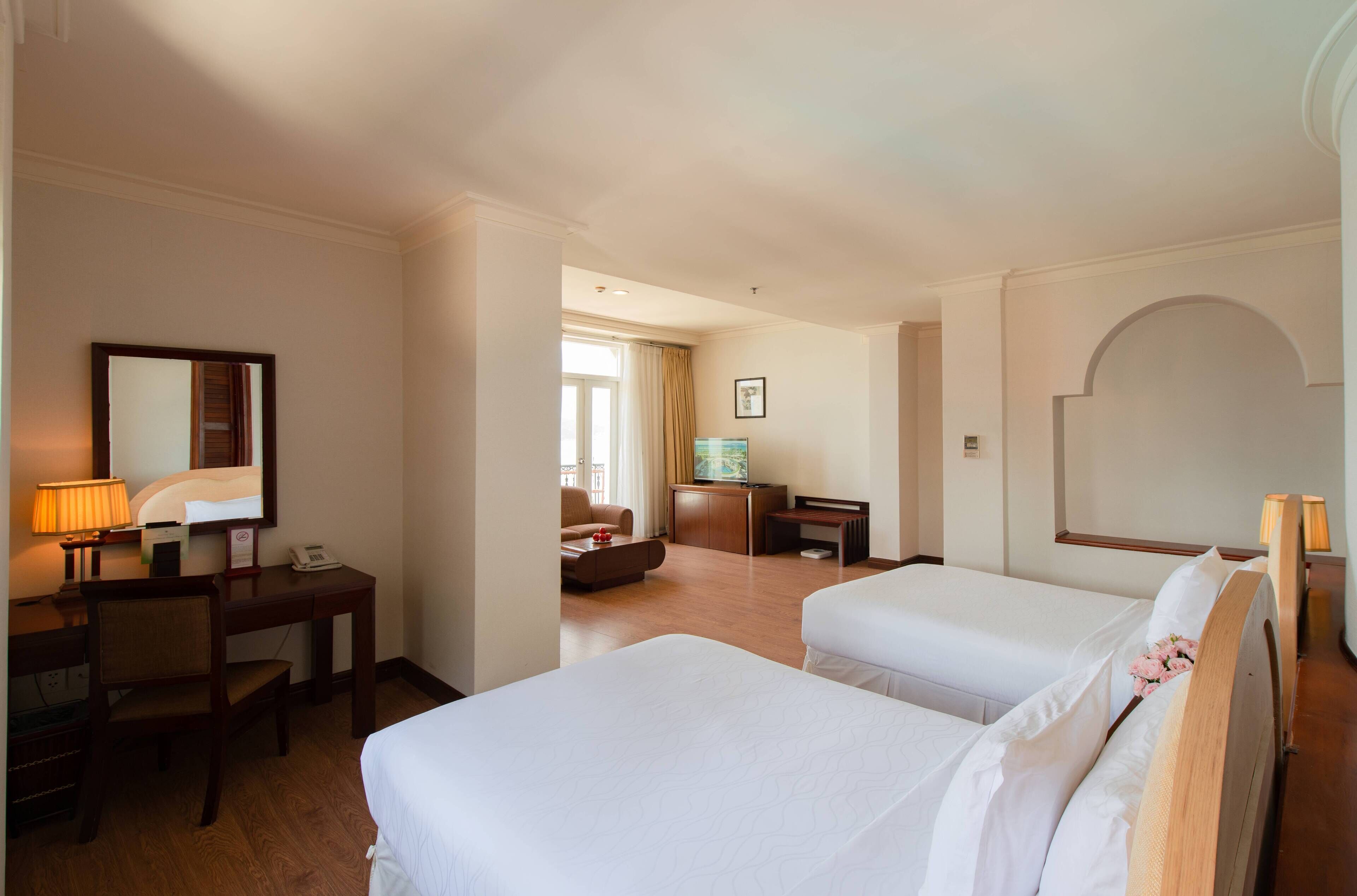 A hotel room with two beds, a desk, a chair, a television, and a mirror.