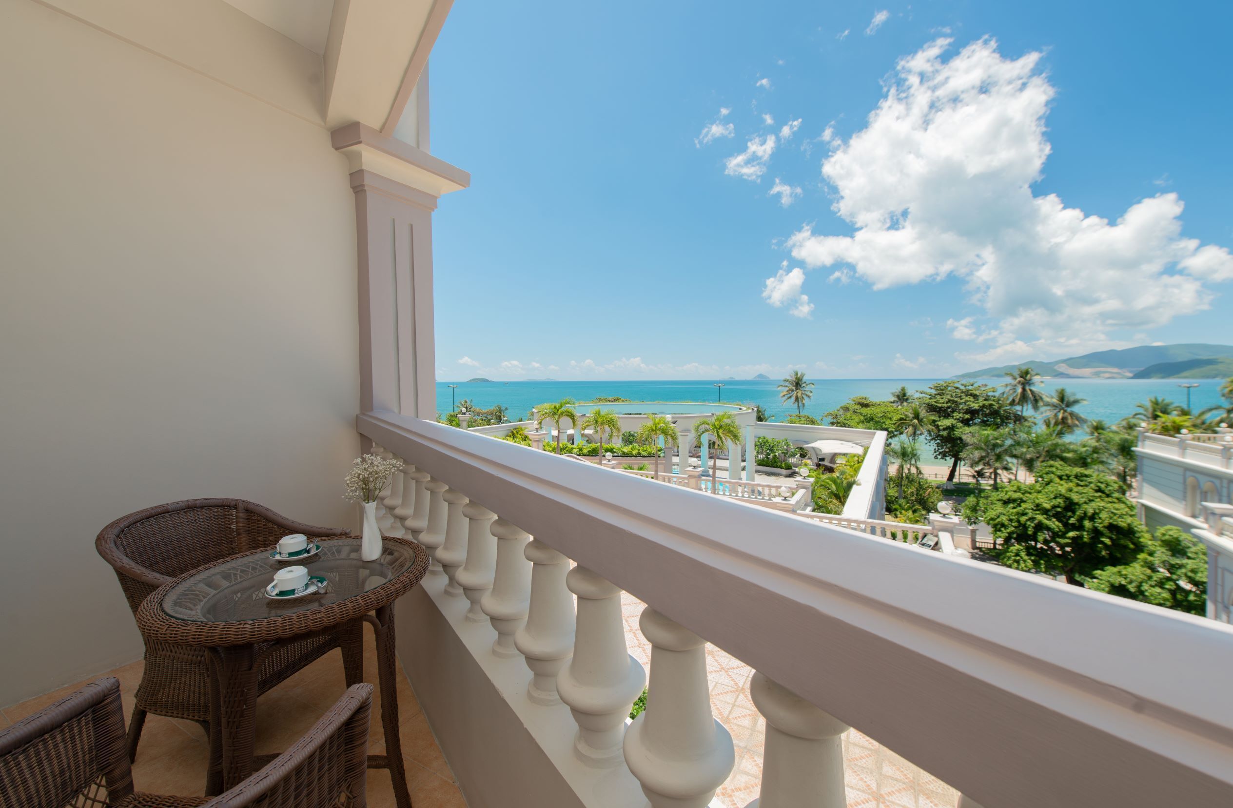 A balcony with wicker furniture, a view of the ocean, and a tropical landscape.