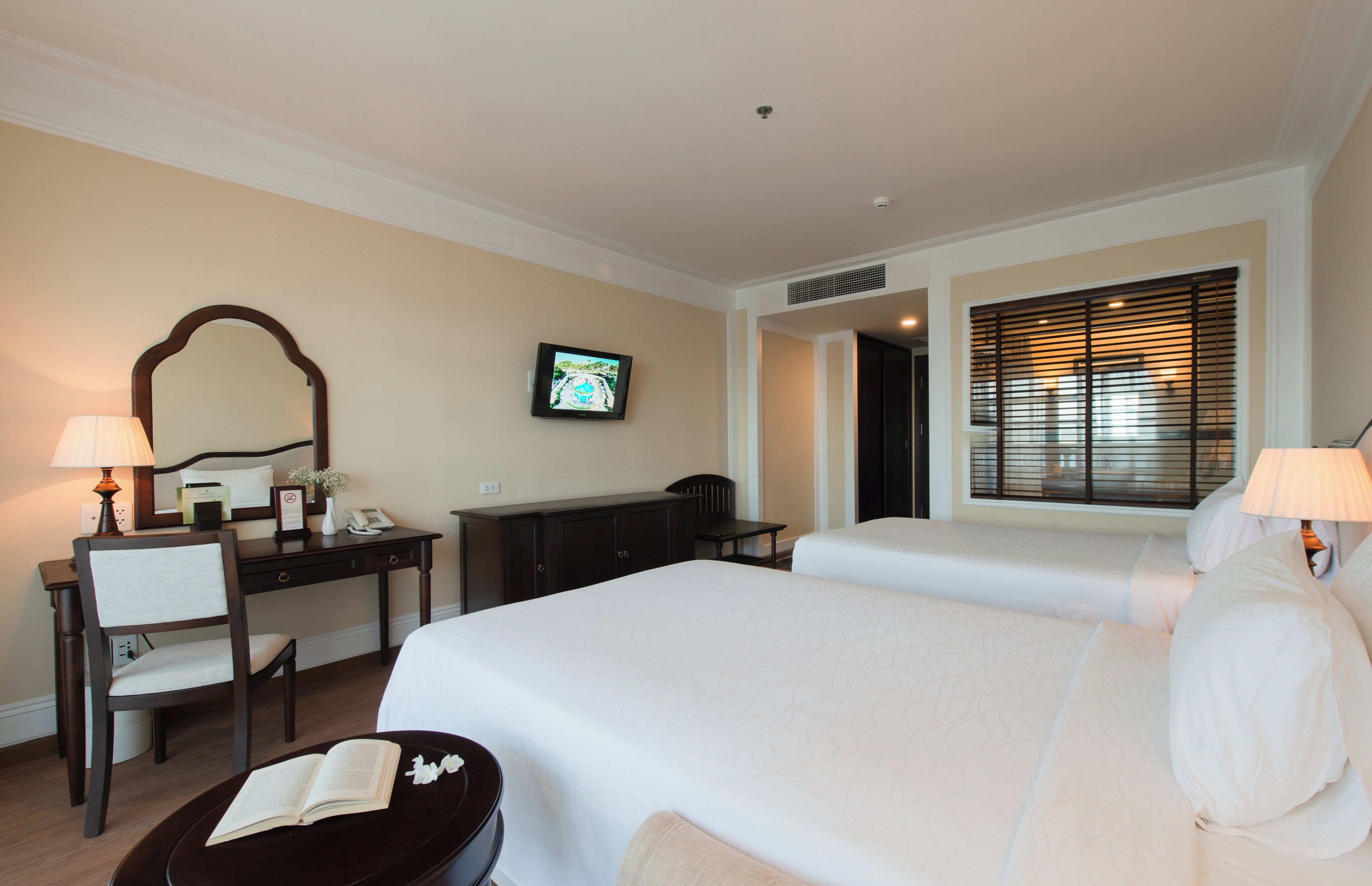 Habitación de hotel con dos camas, un escritorio con silla, televisión y ventana con persianas.
