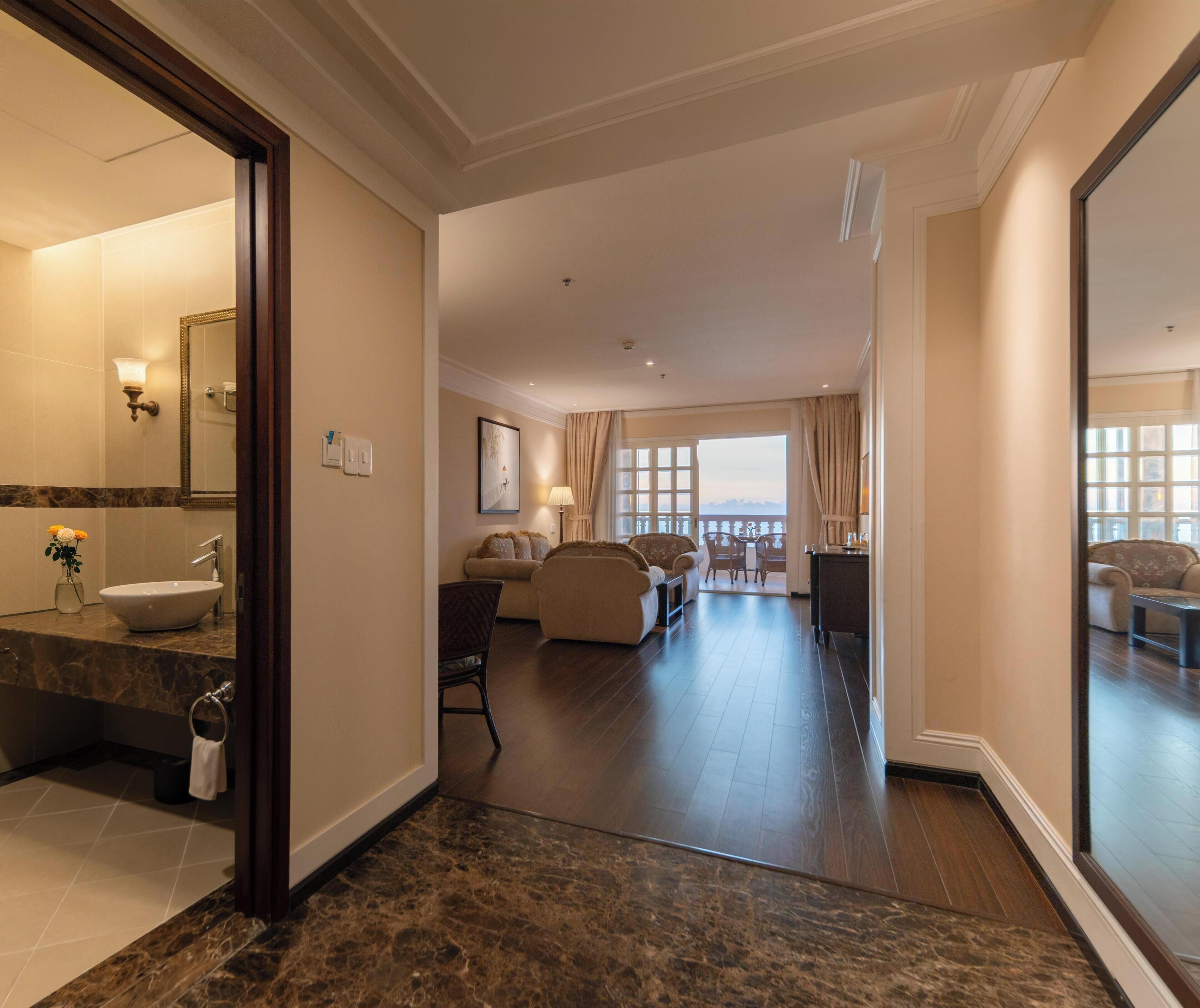 A hotel room with a bathroom, a living area with a sofa and a dining table, and a balcony with a view.