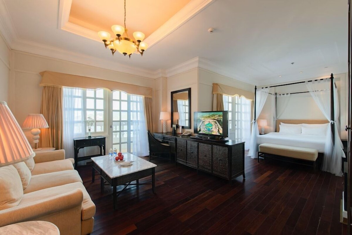 A hotel room with a large bed, a television, a sofa, a coffee table, and a dining table.
