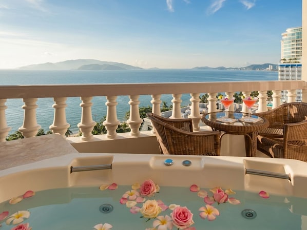 A balcony with a hot tub, wicker chairs, and a table with drinks.