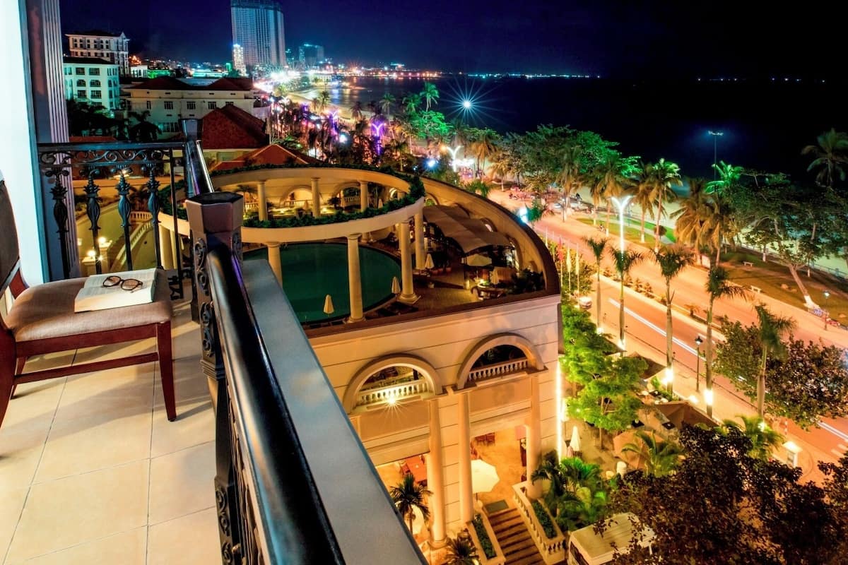 A balcony with a chair, a pool, and a view of a cityscape at night.