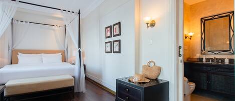 A bedroom with a canopy bed, a bedside table with a lamp, and a view into the bathroom.