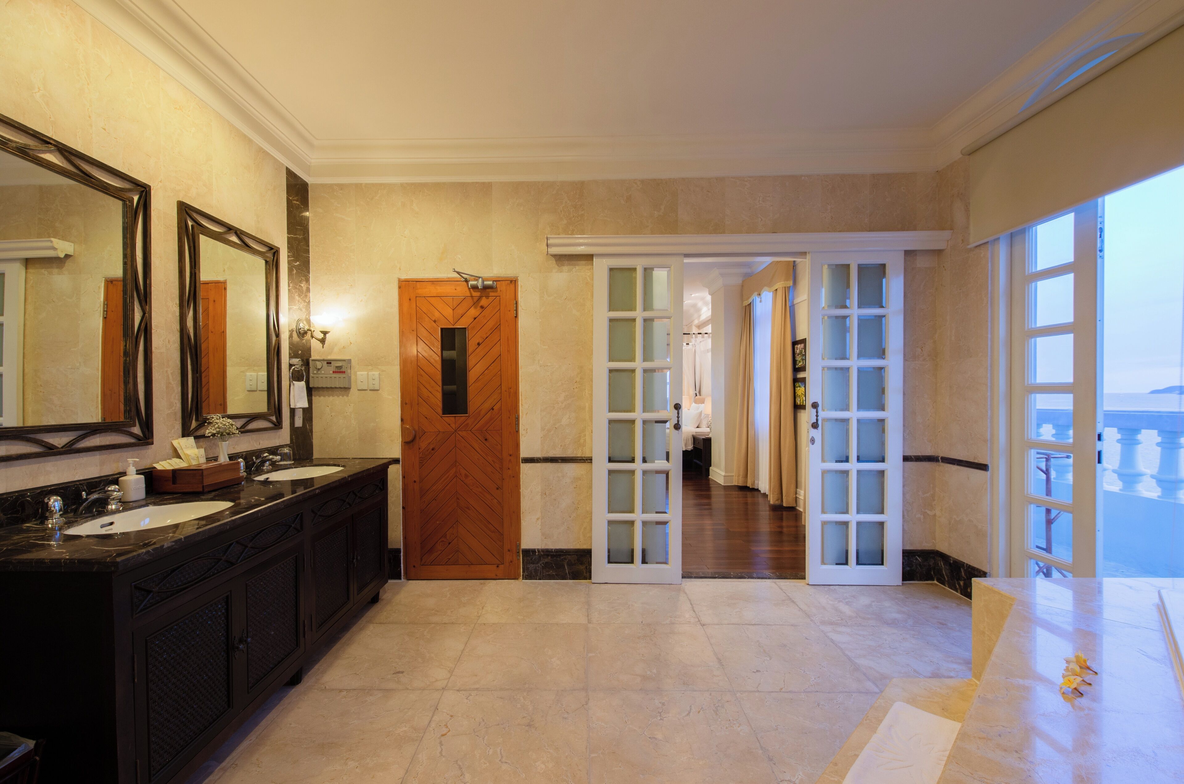 A spacious bathroom with two sinks, a large mirror, and a wooden door leading to a hallway.