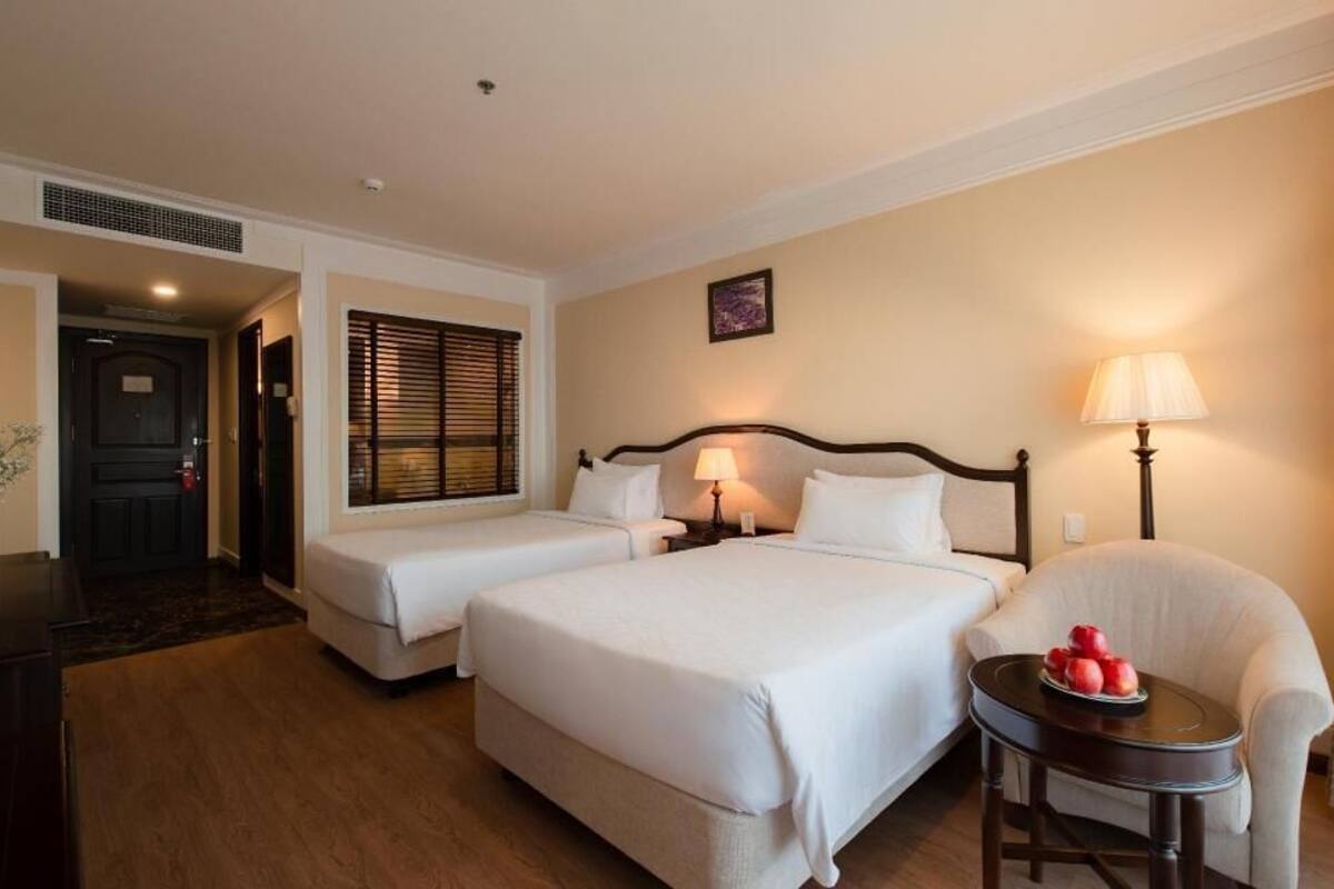 A hotel room with two beds, a chair, a small table, and a door leading to another room.