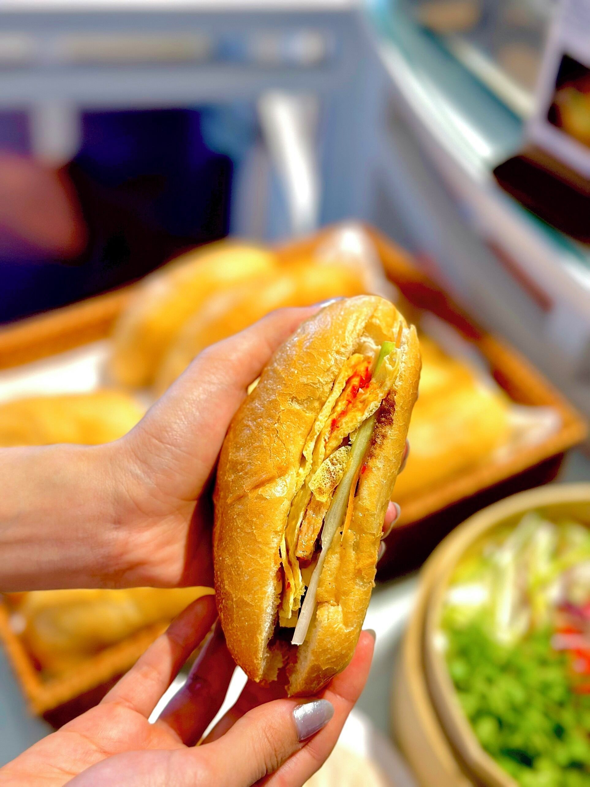 A sandwich held in hands, with a blurred background suggesting a food setting.