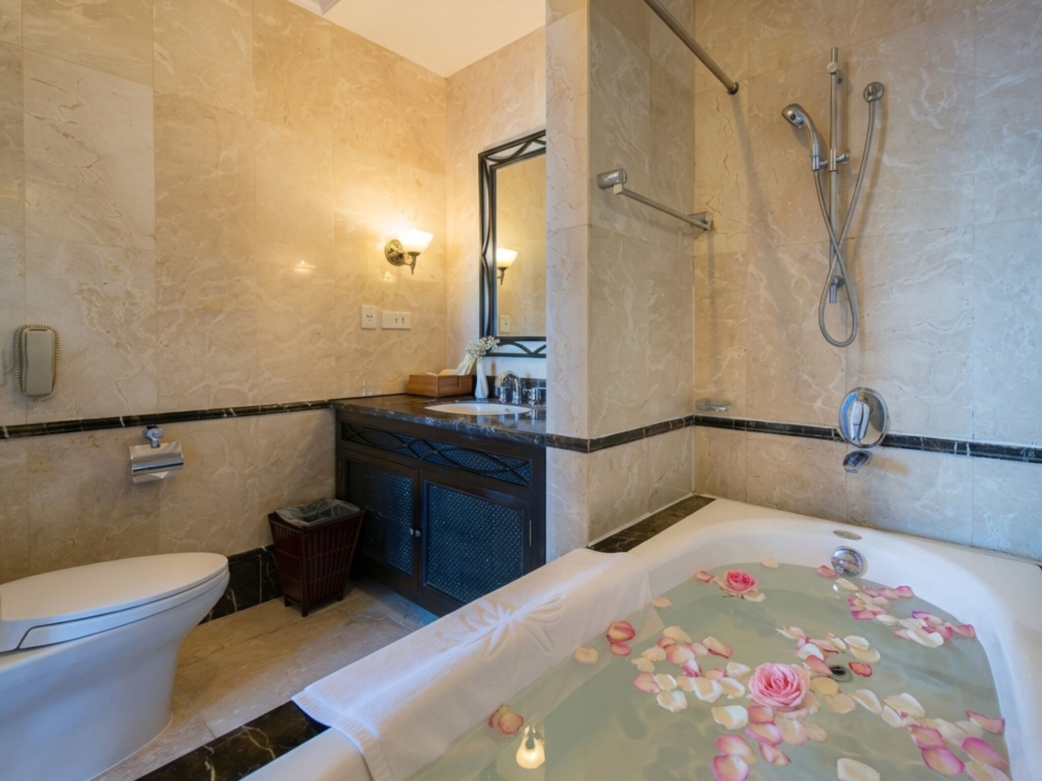Baño con inodoro, lavamanos, espejo, ducha y bañera con pétalos de rosa.