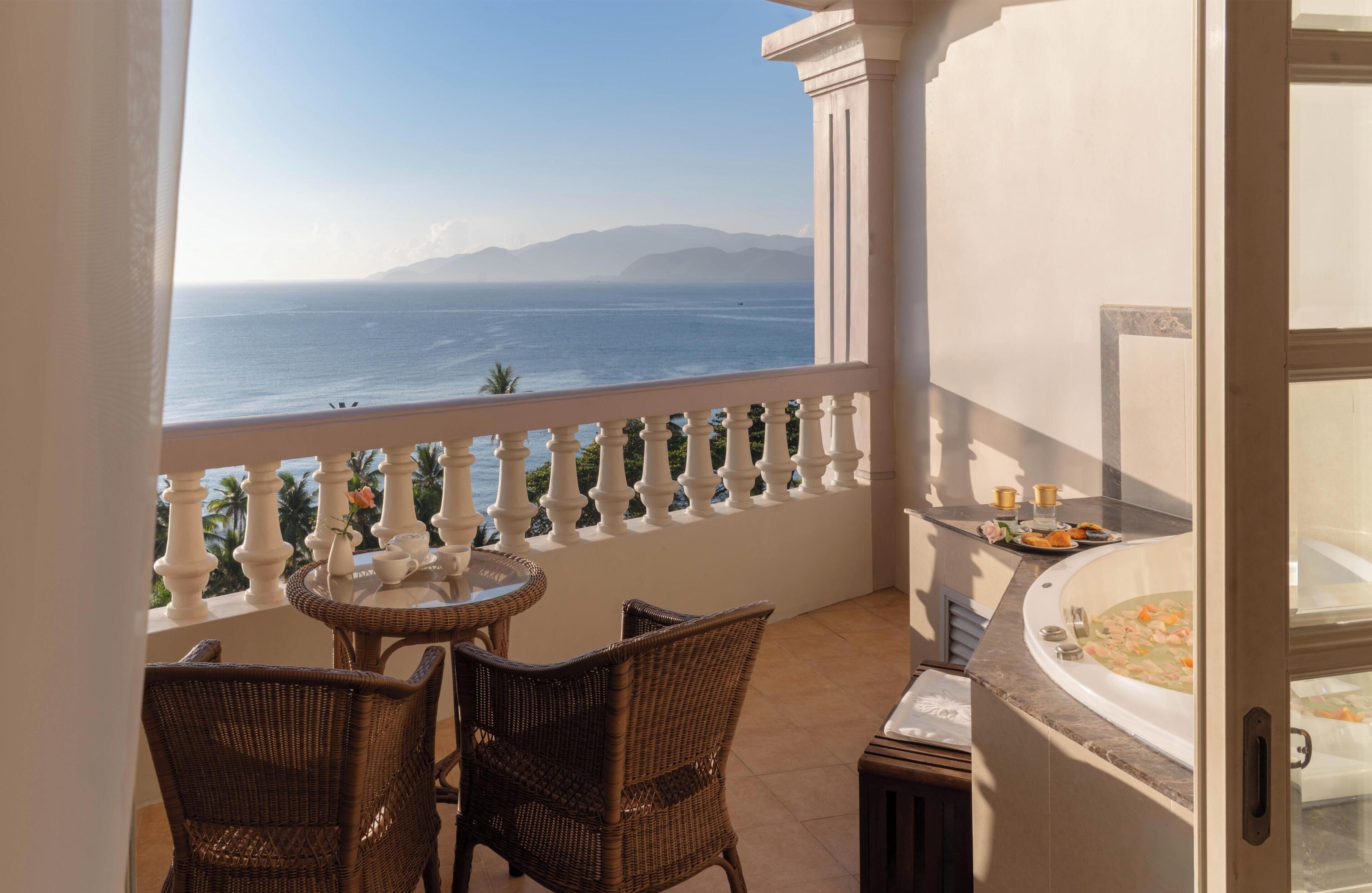 Ein Balkon mit Korbstühlen, einem kleinen runden Tisch, einer Badewanne und Blick aufs Meer.