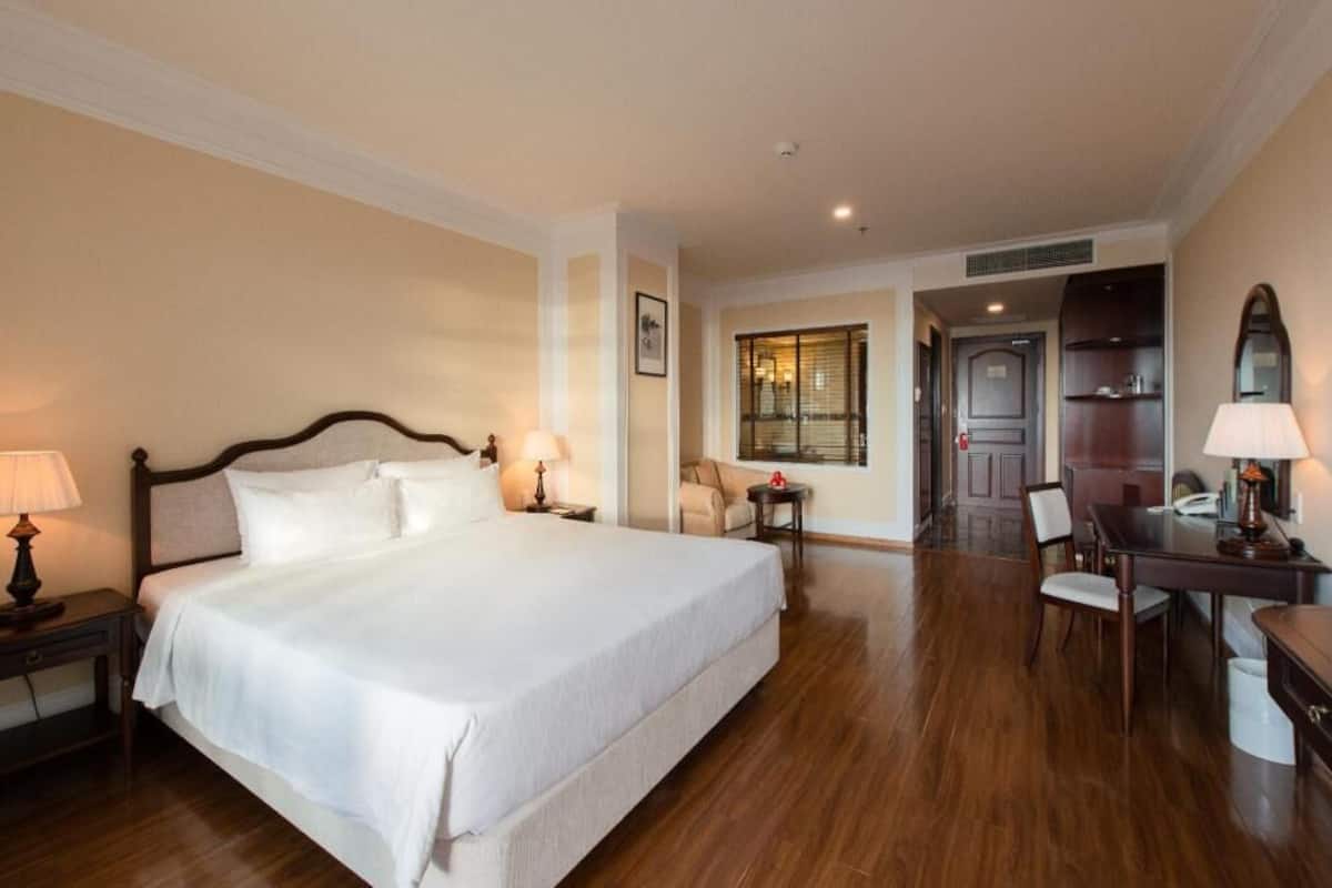 A hotel room with a large bed, bedside lamps, a desk with a chair, and a view of the outside.