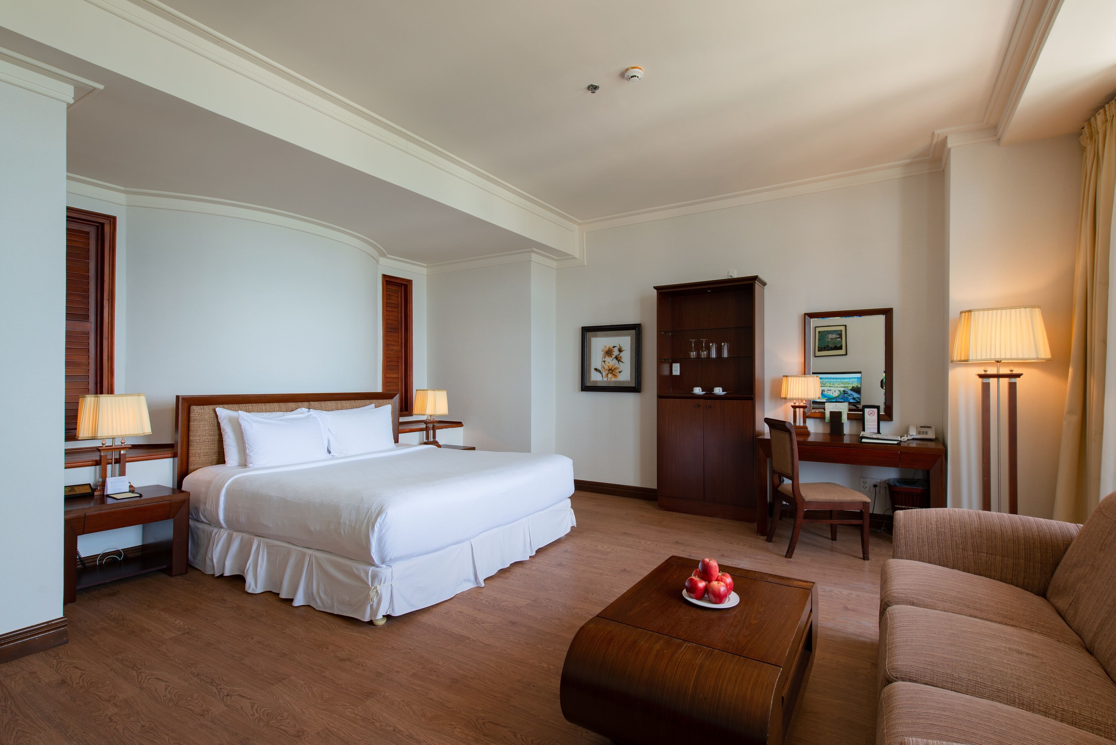 Une chambre d’hôtel avec un grand lit, un bureau avec une chaise, un canapé et une petite table avec des fruits.