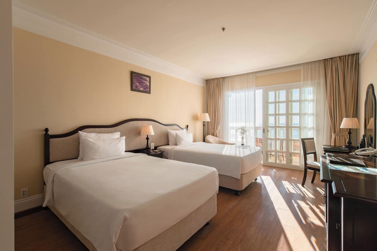 A hotel room with two beds, a desk, a chair, and a large window with curtains.