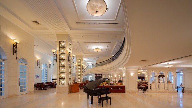 Un vestíbulo amplio con un piano de cola, candelabros elegantes y una escalera curva.