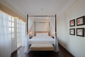 Una cama con dosel y cortinas blancas, un banco de madera y vistas al exterior a través de amplios ventanales.