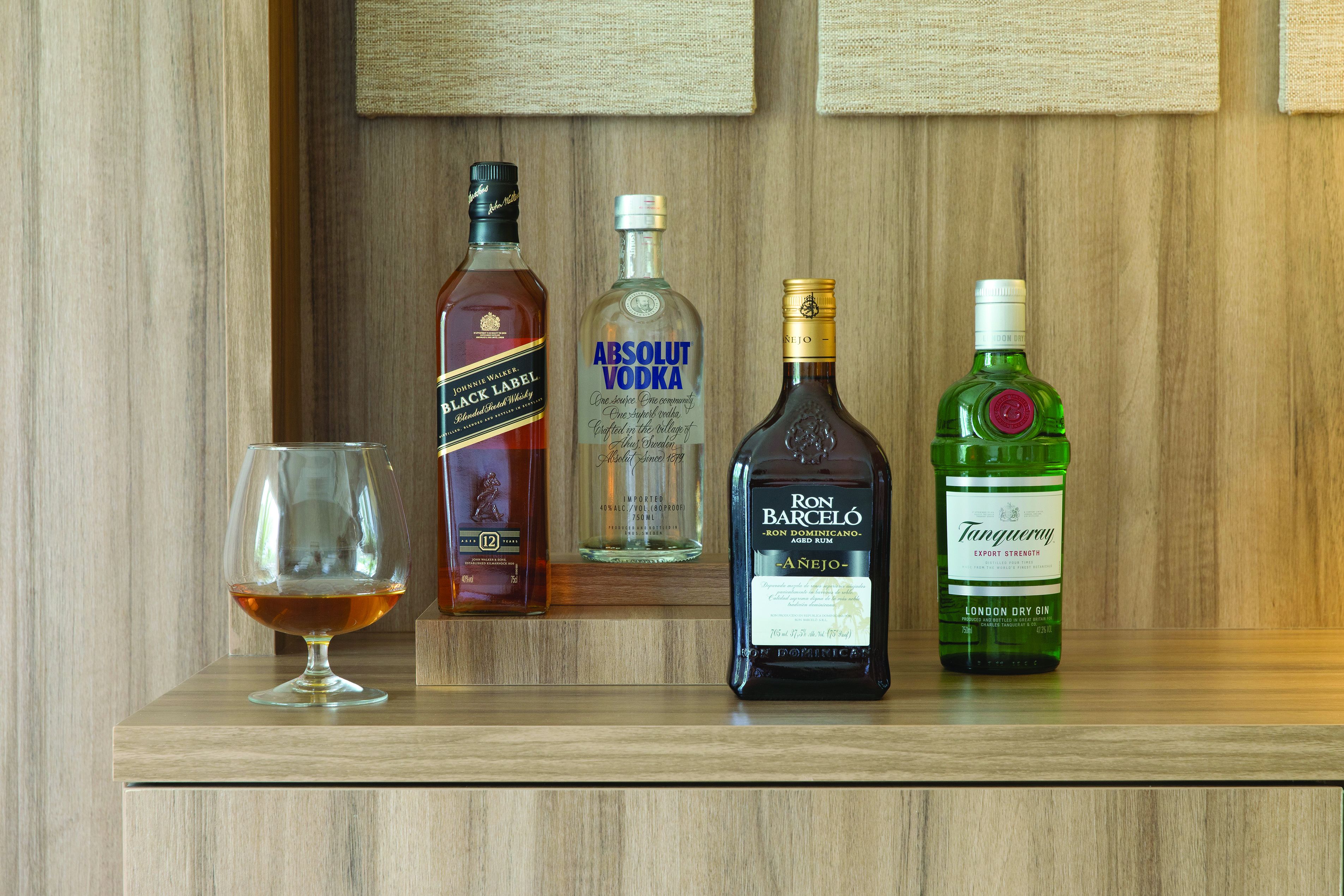 Una estantería de madera con cuatro botellas de licor y una copa.