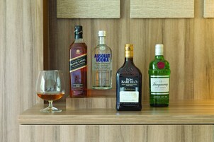 Una estantería de madera con cuatro botellas de licor y una copa.