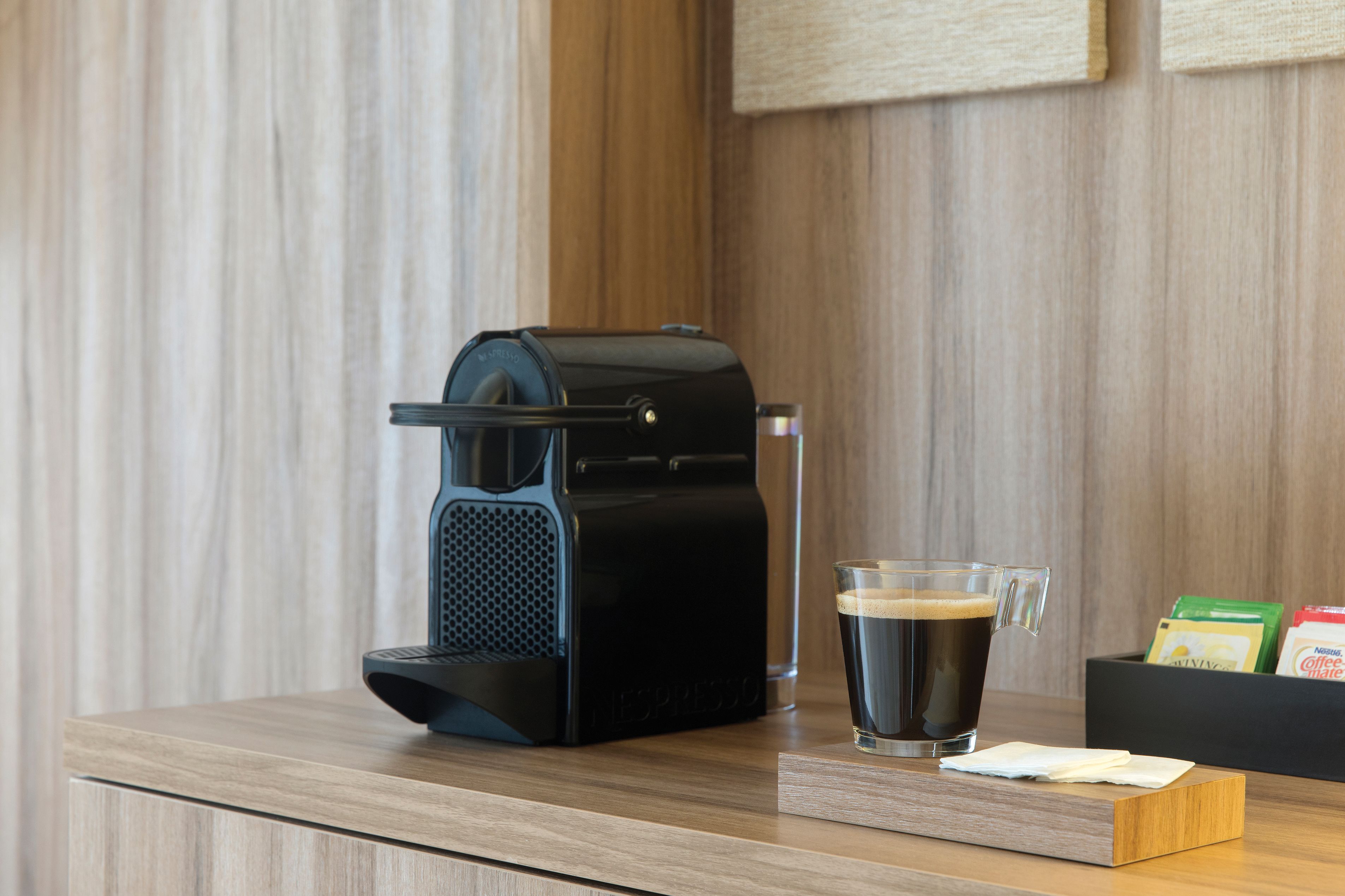 Een koffiezetapparaat op een houten aanrecht, met een glas koffie en koffiepads.