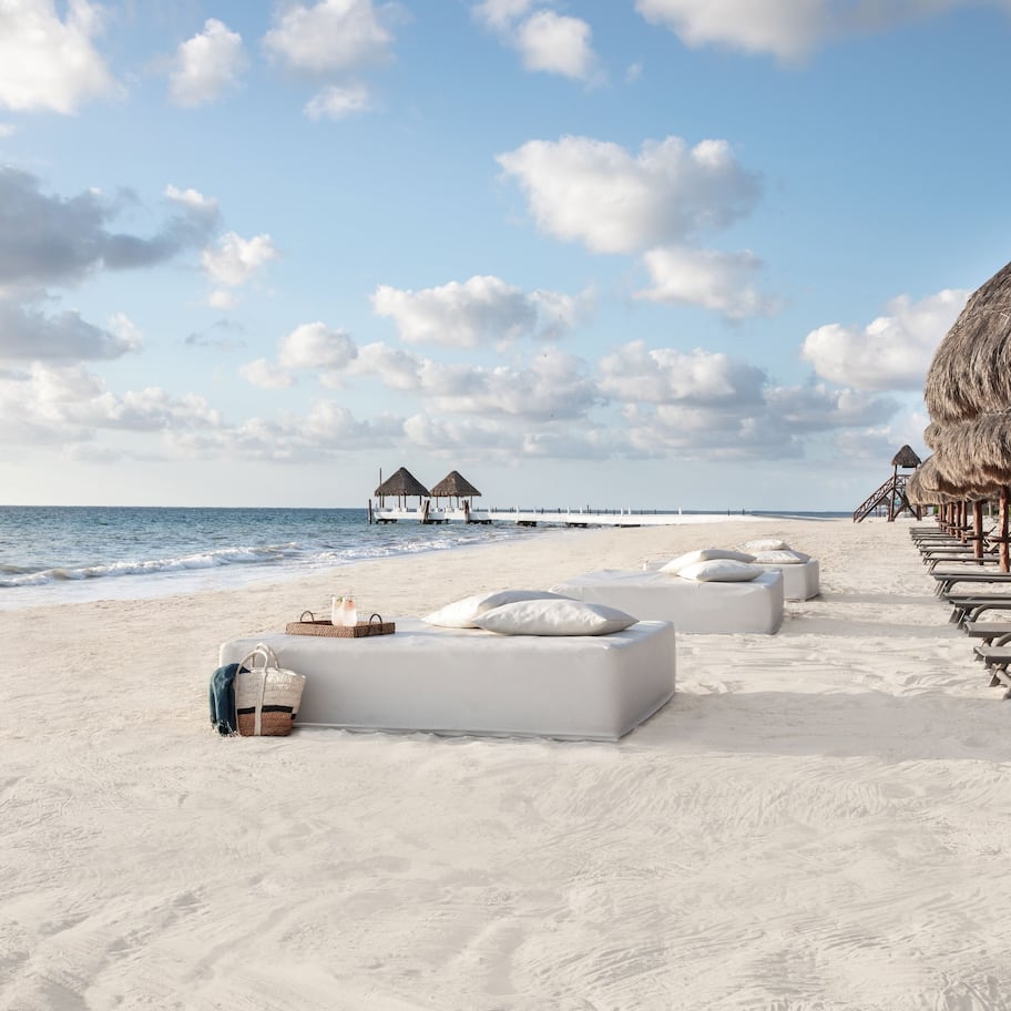 A beach with white lounge chairs and a thatched-roof structure.