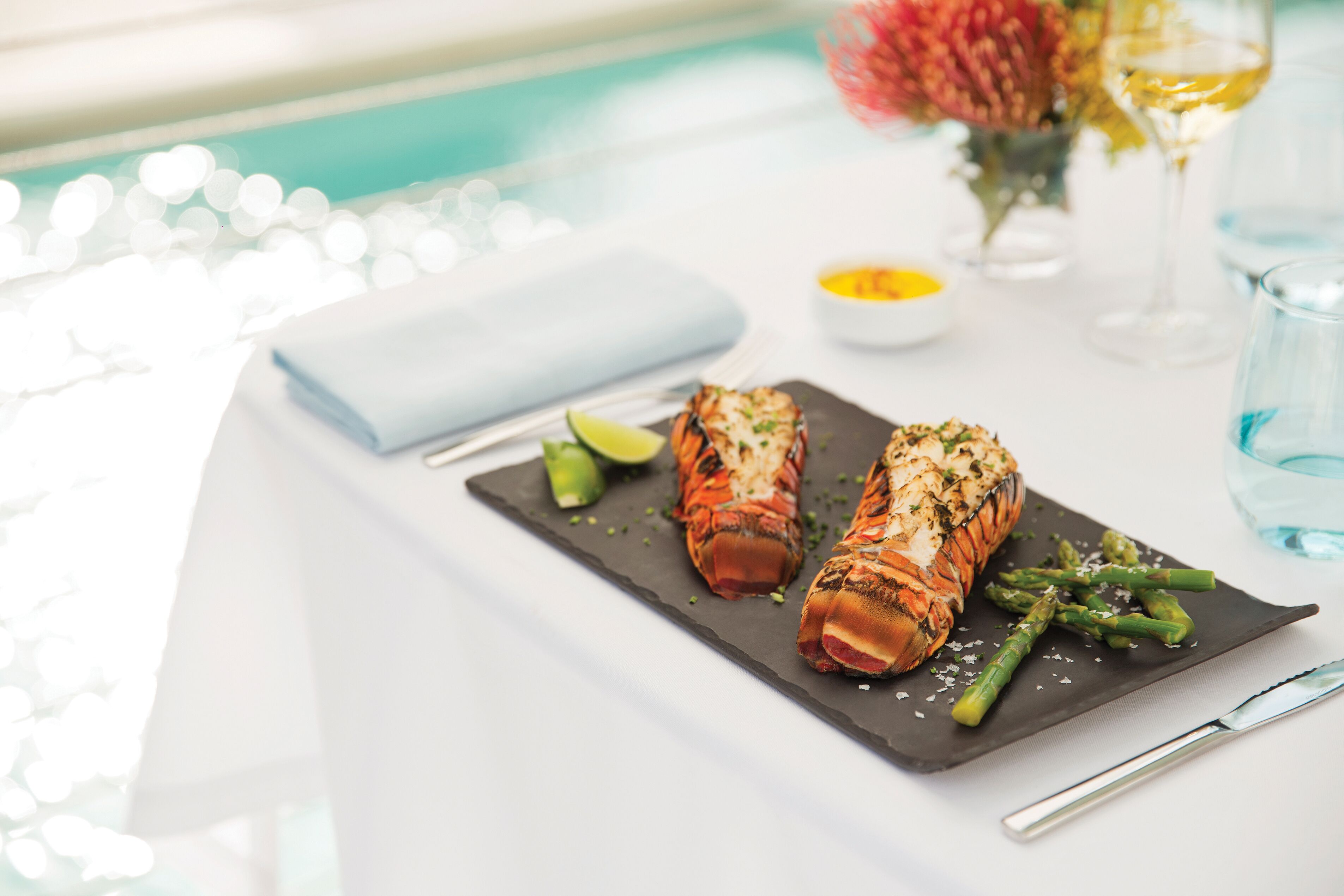 A dining table with a seafood dish, asparagus, and a knife.