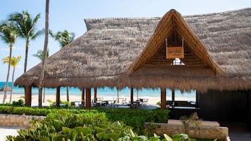 Edificio con techo de paja y un letrero que dice "las Palmas" en una playa con palmeras y cielo despejado.