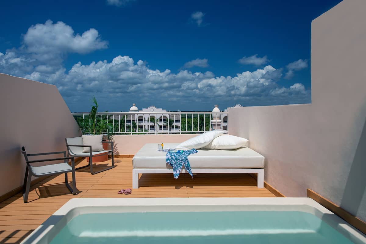 A rooftop terrace with a hot tub, lounge chairs, and a bed with a view of the city skyline.
