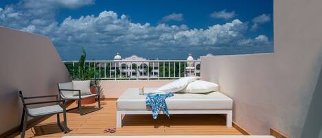 A rooftop terrace with a hot tub, lounge chairs, and a bed with a view of the city skyline.