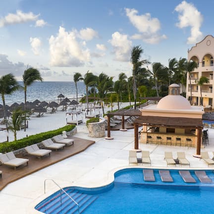 A resort pool area with lounge chairs, a gazebo, and a view of the ocean.