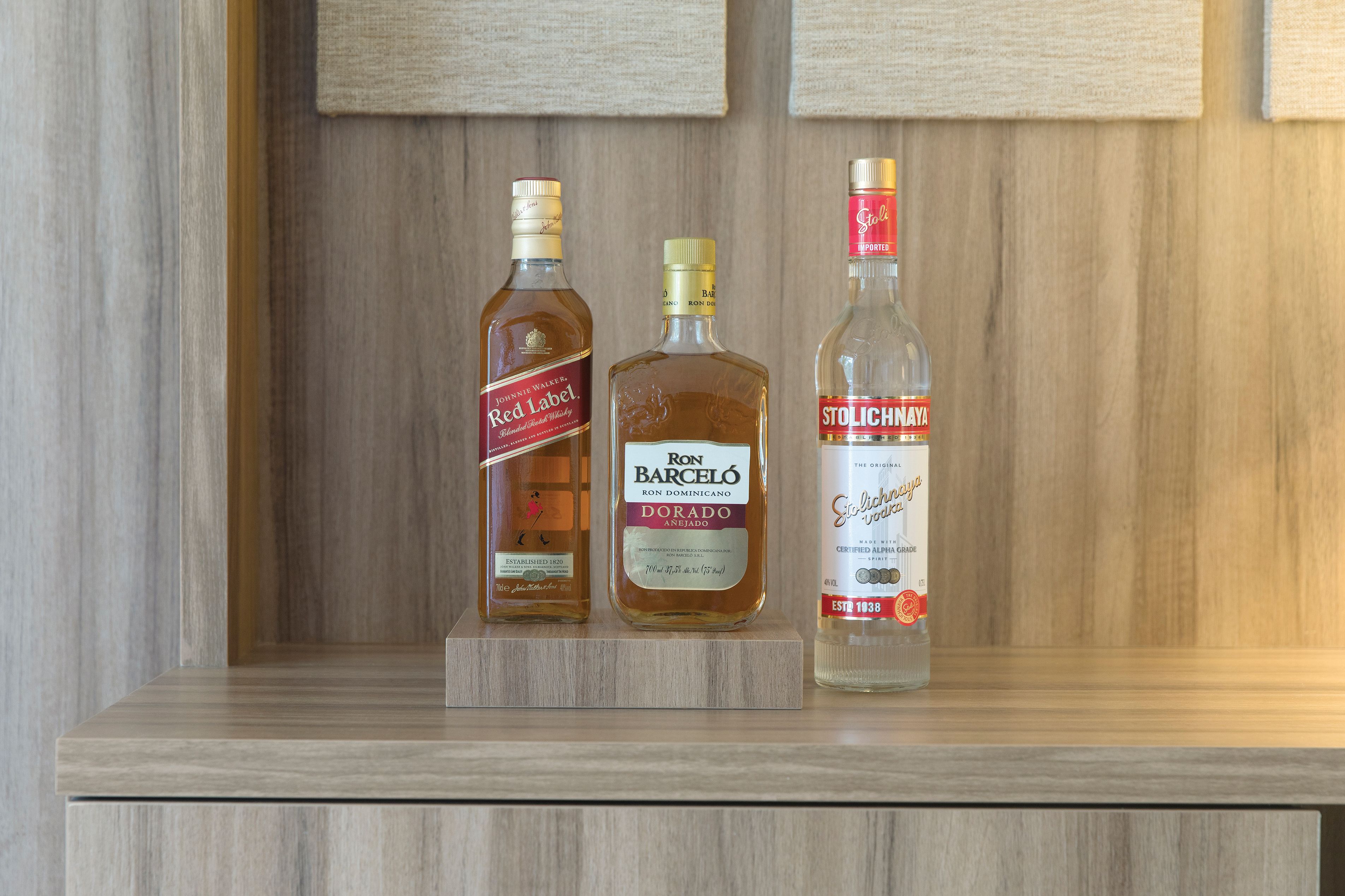 Three bottles of liquor on a wooden shelf.