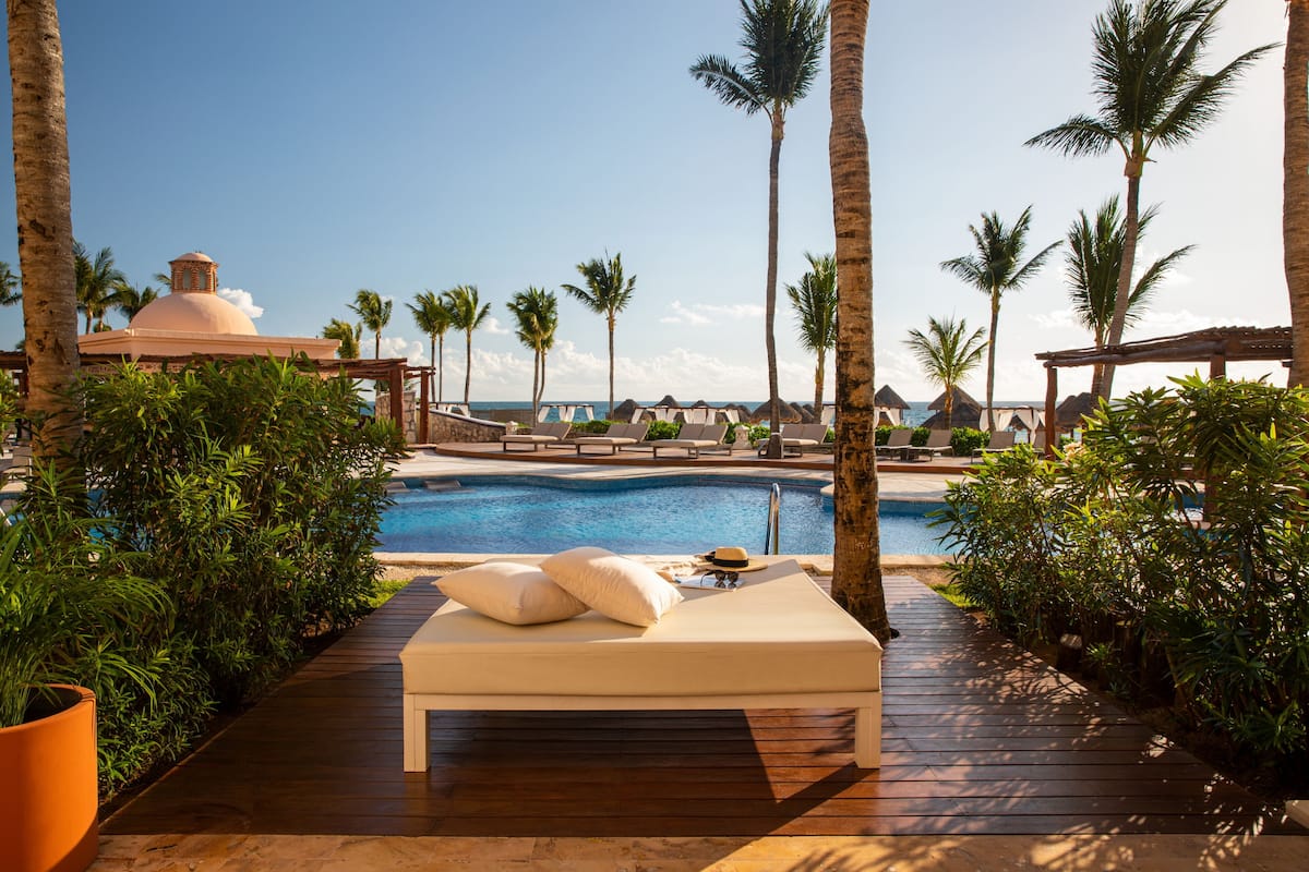 A poolside lounge area with a wooden deck, lounge chairs, and a view of the ocean.