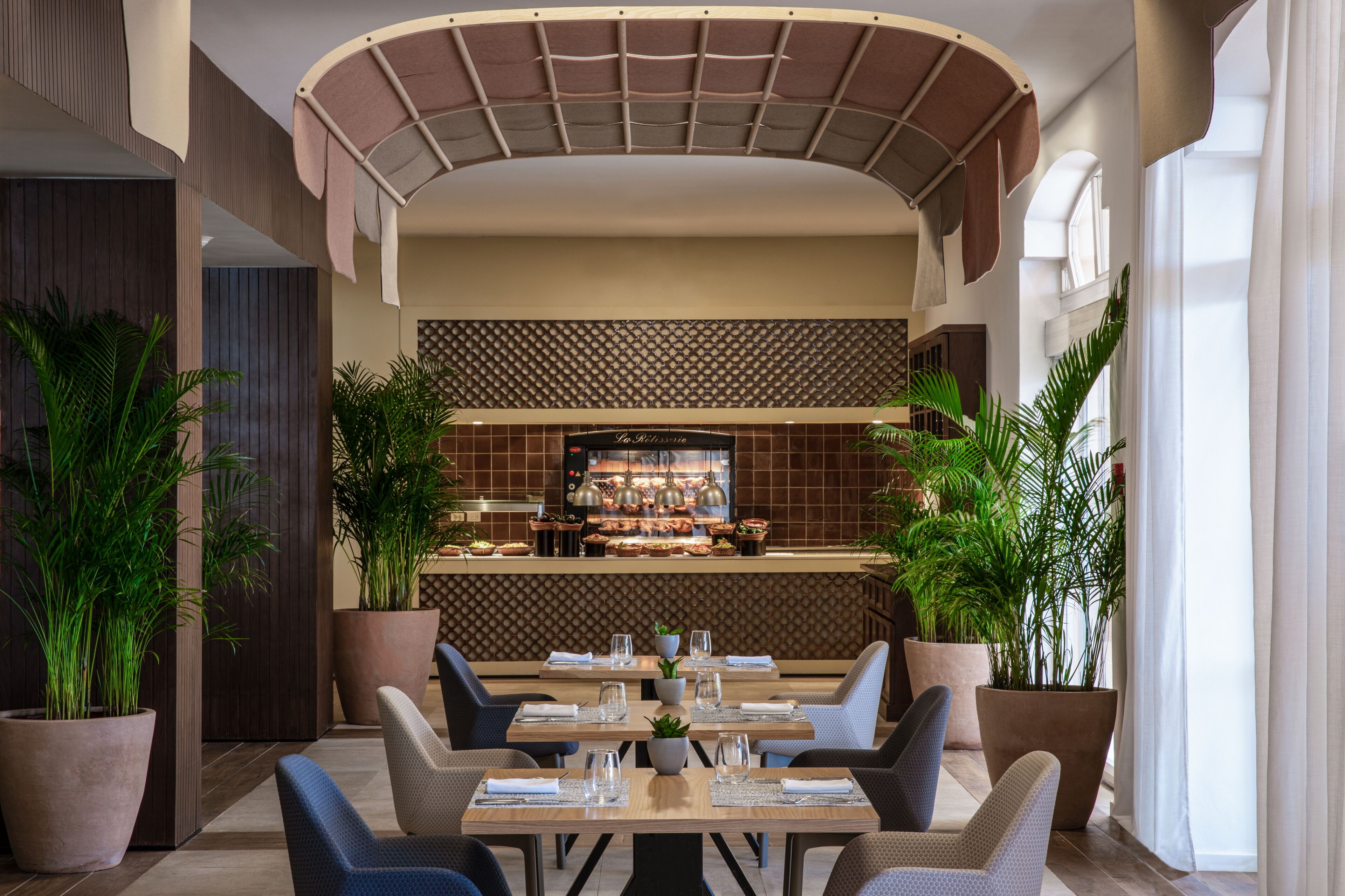 A modern restaurant with a central bar, seating area, and potted plants.