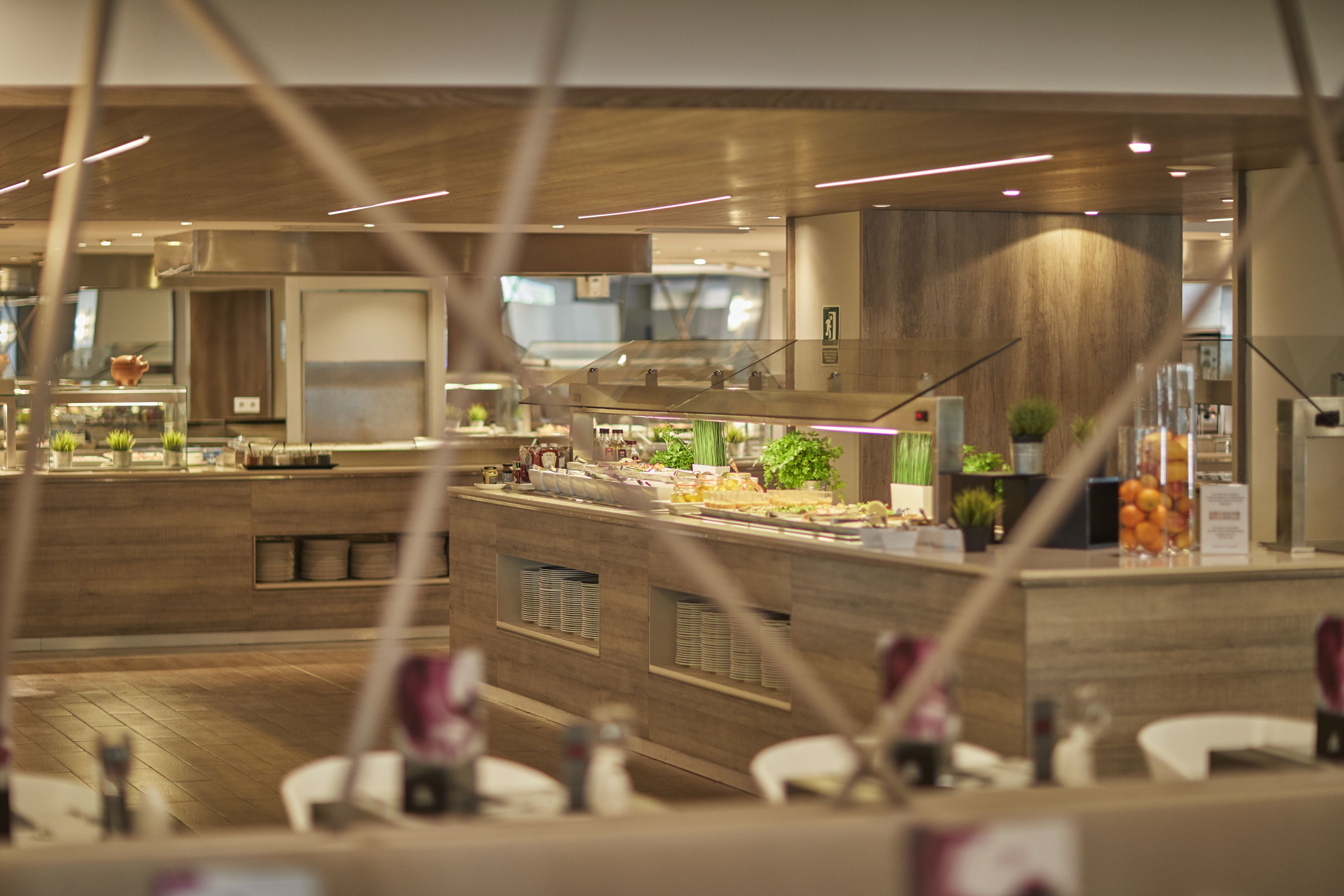 Een modern restaurant met een houten inrichting, meerdere eettafels en diverse etalages met eten.