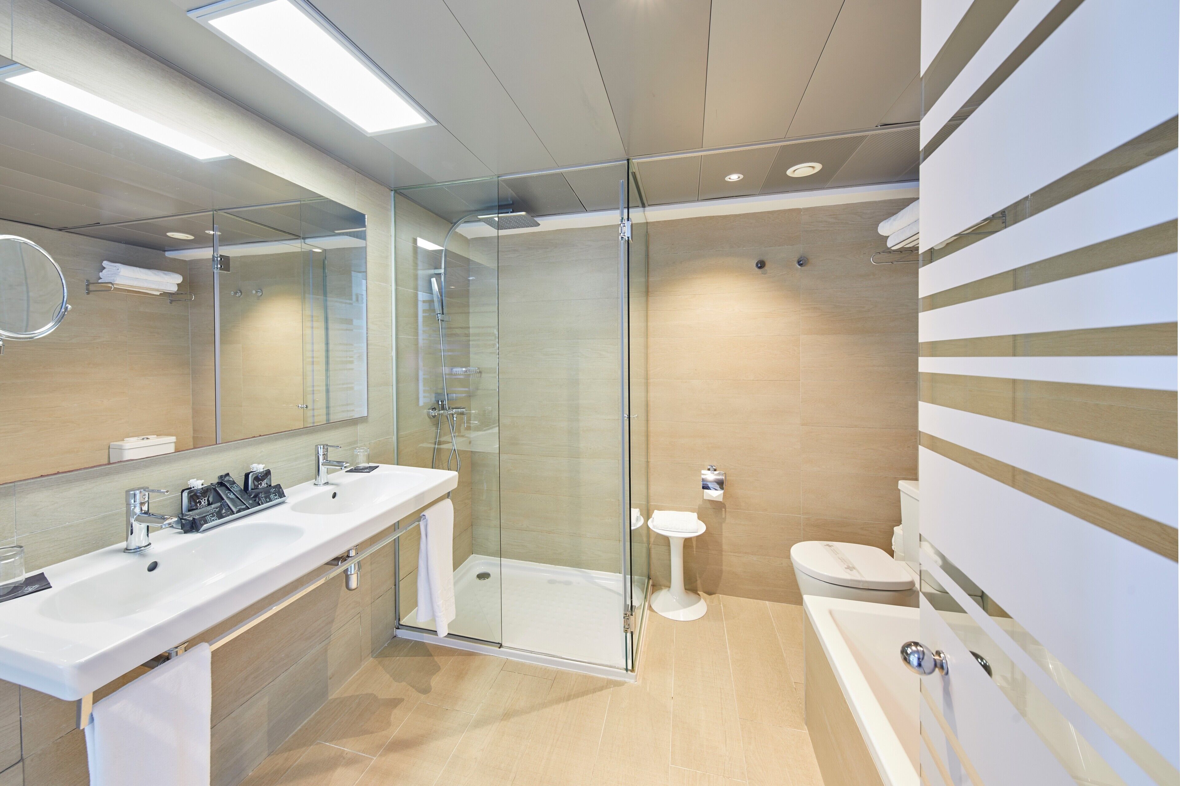 Un baño moderno con ducha envuelta en vidrio, un lavamanos grande con dos grifos, inodoro y bañera.