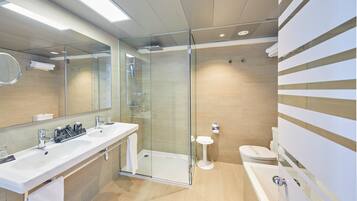 Un baño moderno con ducha envuelta en vidrio, un lavamanos grande con dos grifos, inodoro y bañera.