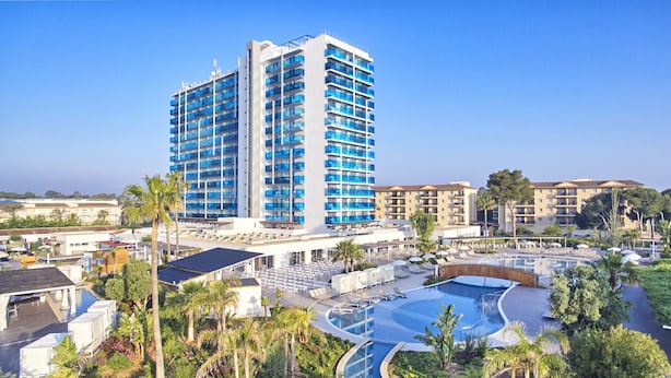 Un hotel con una piscina grande, varios balcones y un jardín circundante.