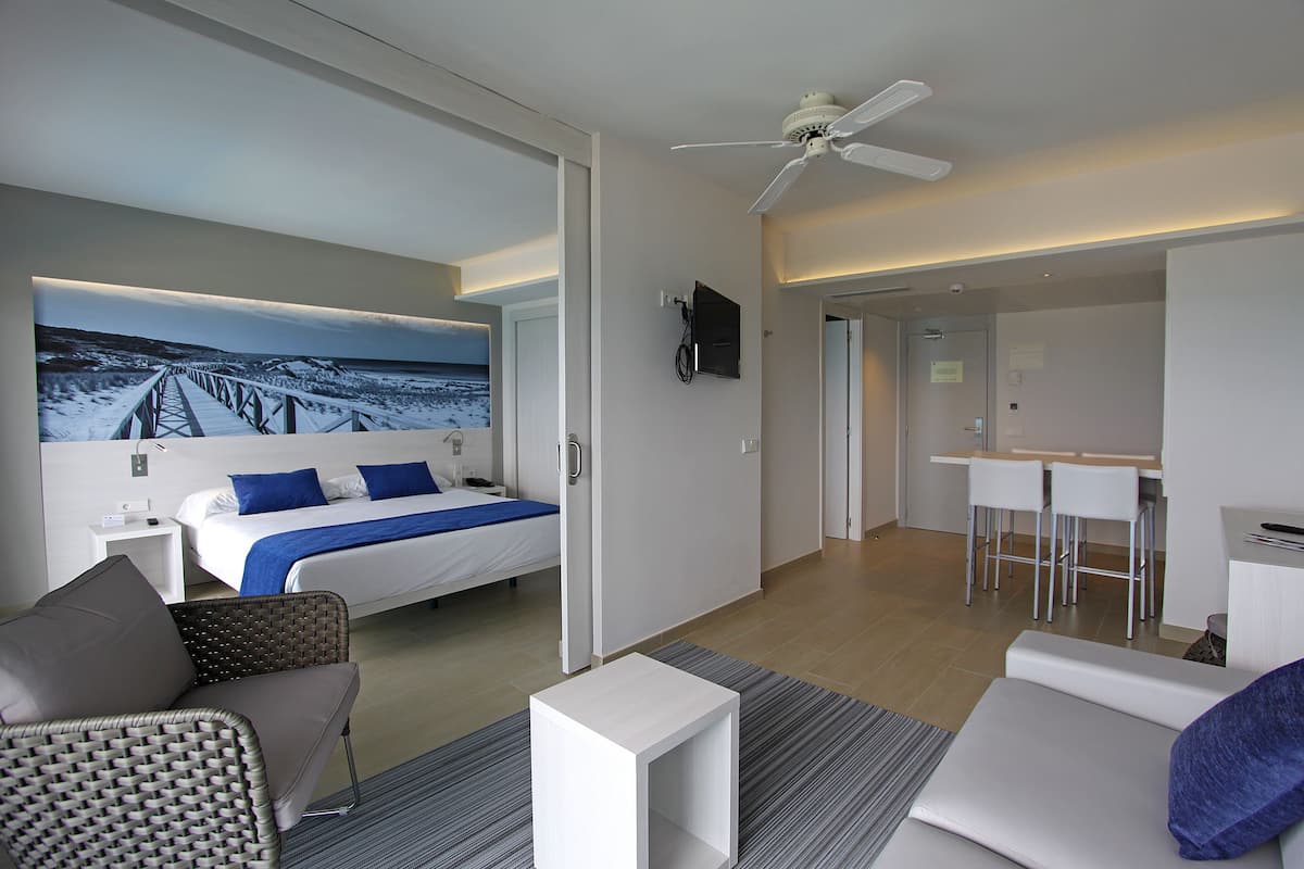 A modern hotel room with a bed, a seating area, a desk, and a view of a snowy landscape through a large window.