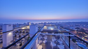 Una terraza en la azotea con mobiliario exterior y vistas a la ciudad al anochecer.