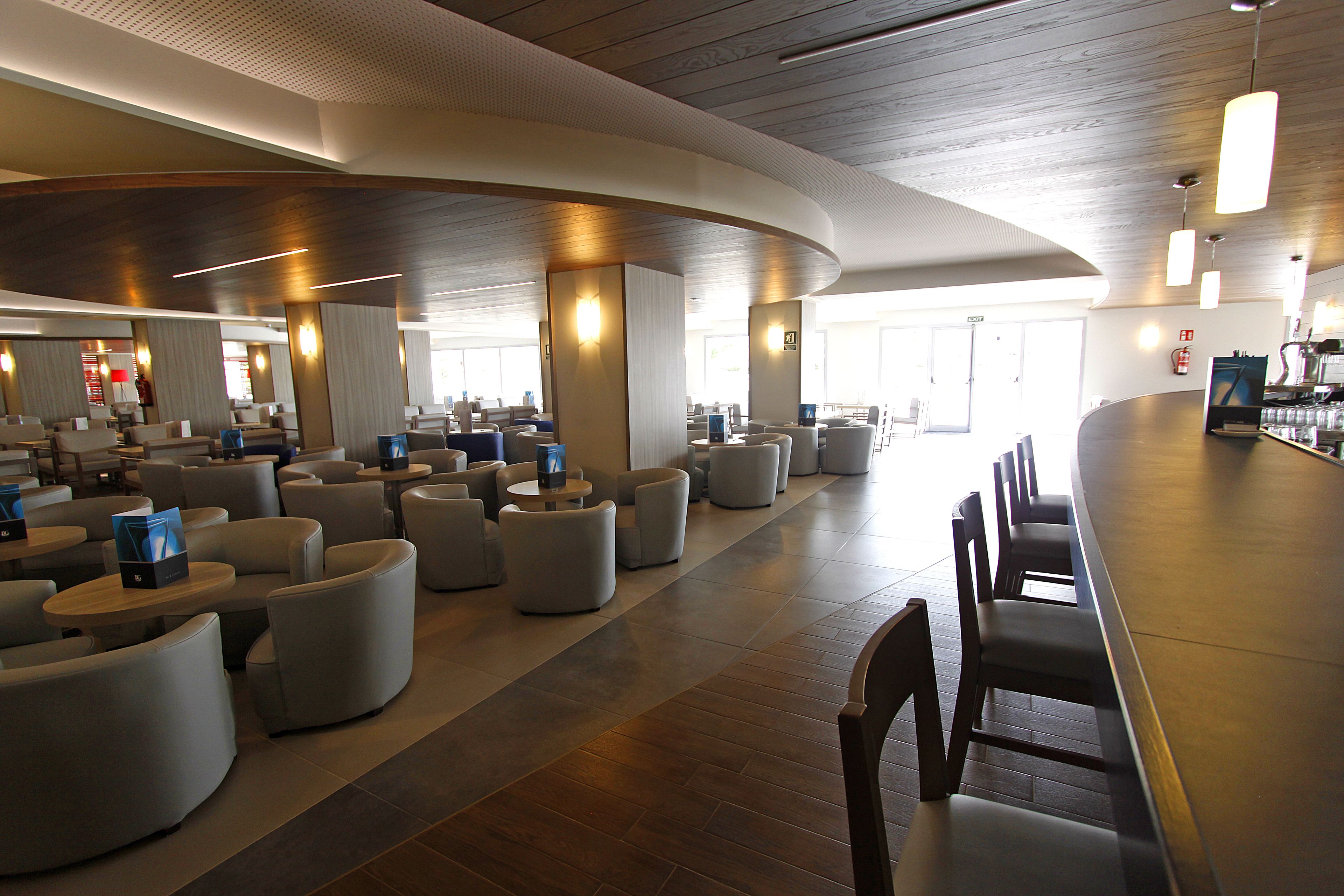 Un hall d’hôtel moderne avec des espaces de détente aux lignes courbes, un bar et un grand miroir qui reflète l’espace.