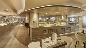 Un restaurante moderno con una barra central que exhibe diferentes alimentos, rodeado de sillas y mesas blancas.