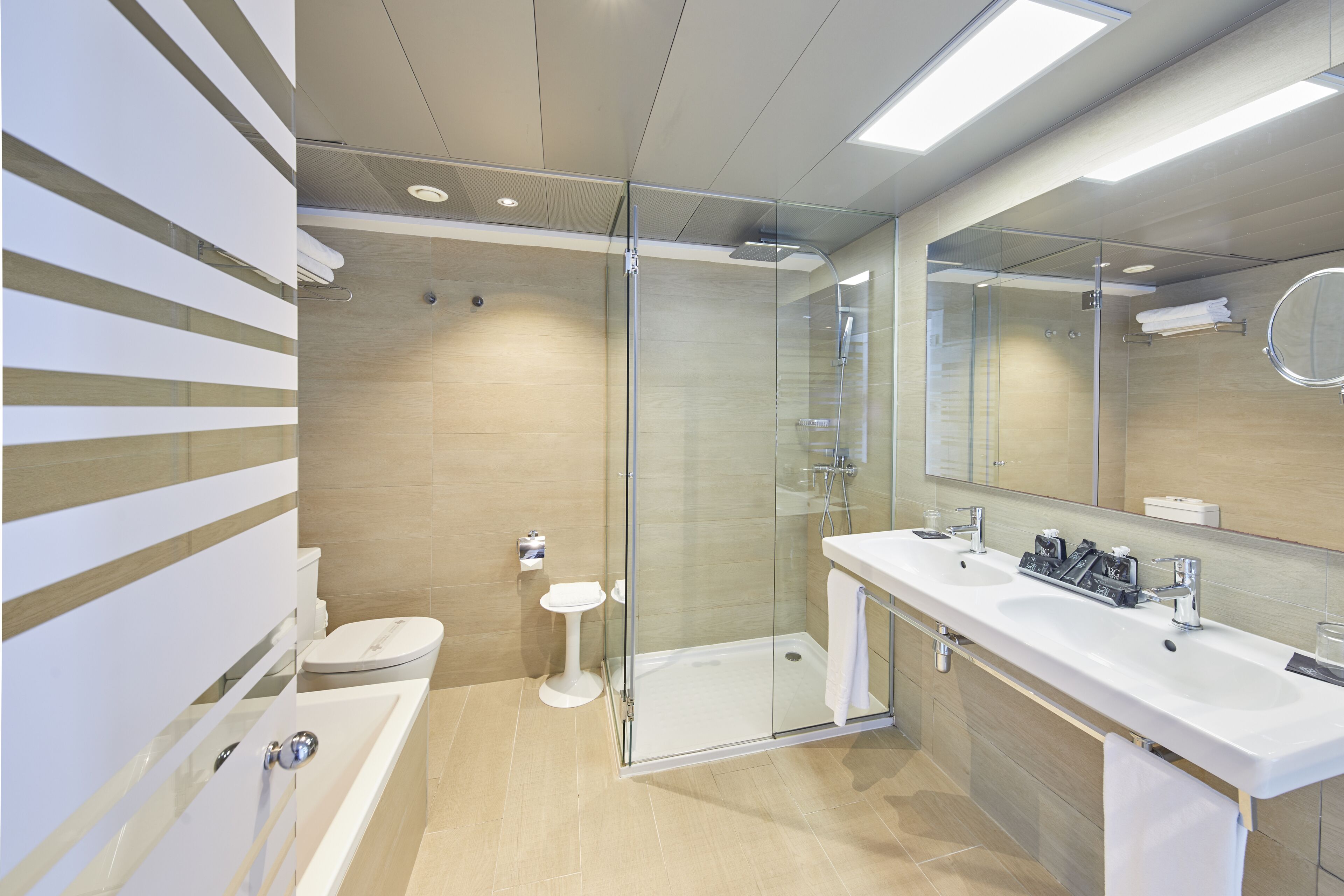 Un baño moderno con ducha de vidrio, lavamanos blanco y un espejo grande.