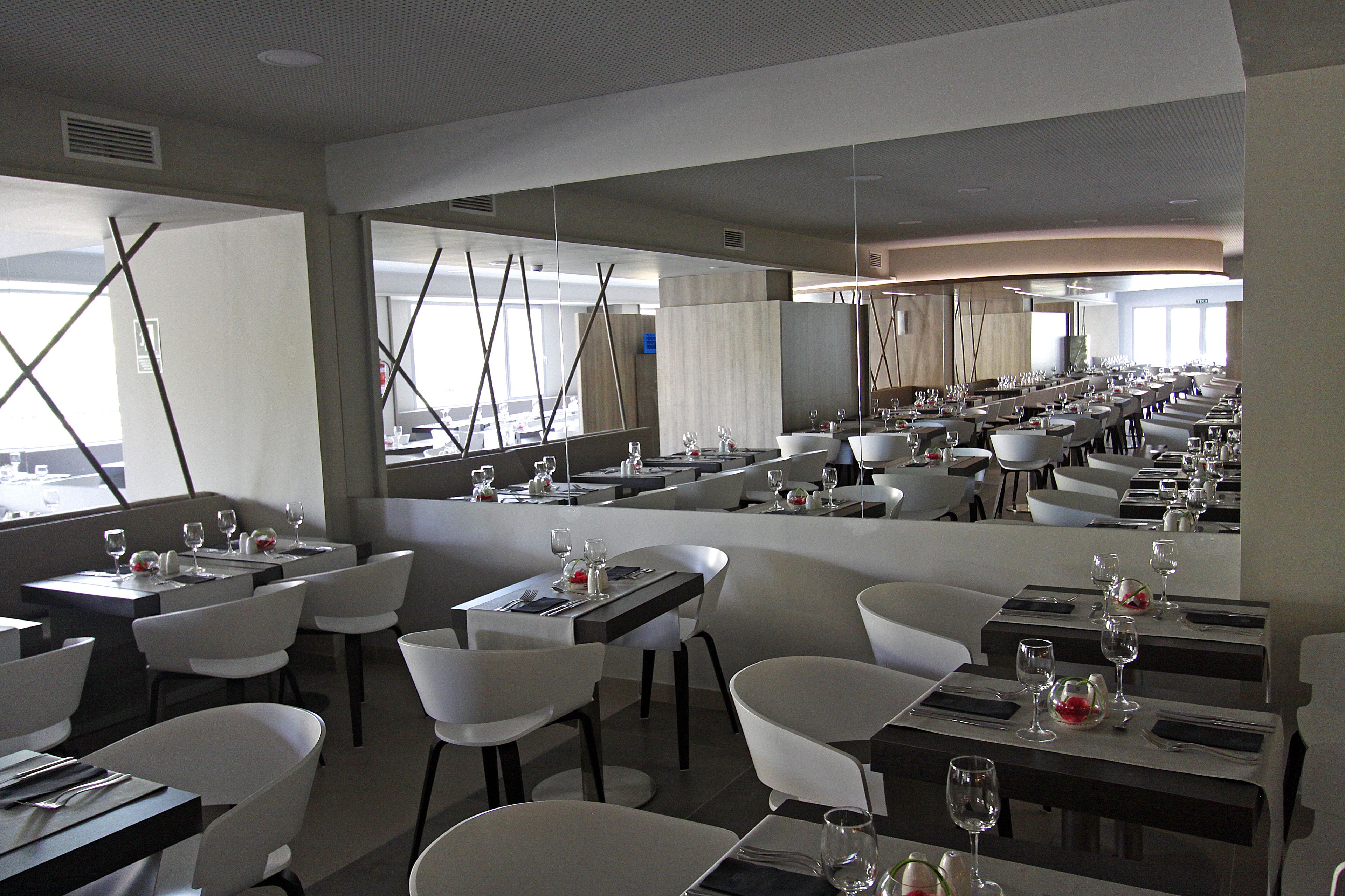 Un restaurant moderne avec des chaises et des tables blanches, de grandes fenêtres et une vue sur l’extérieur.