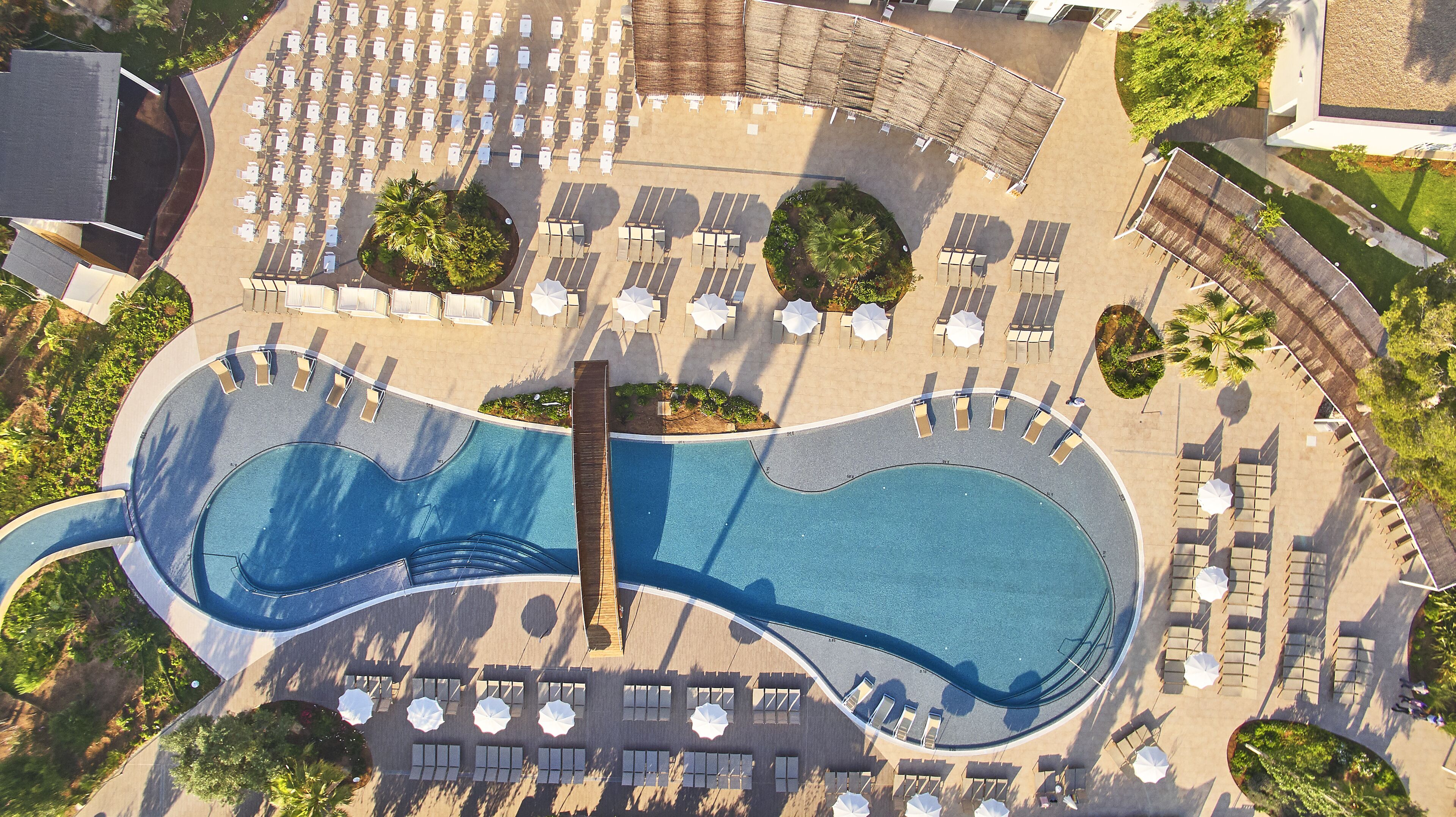 Vista aérea de un resort con una piscina grande, tumbonas y zonas con sombra.