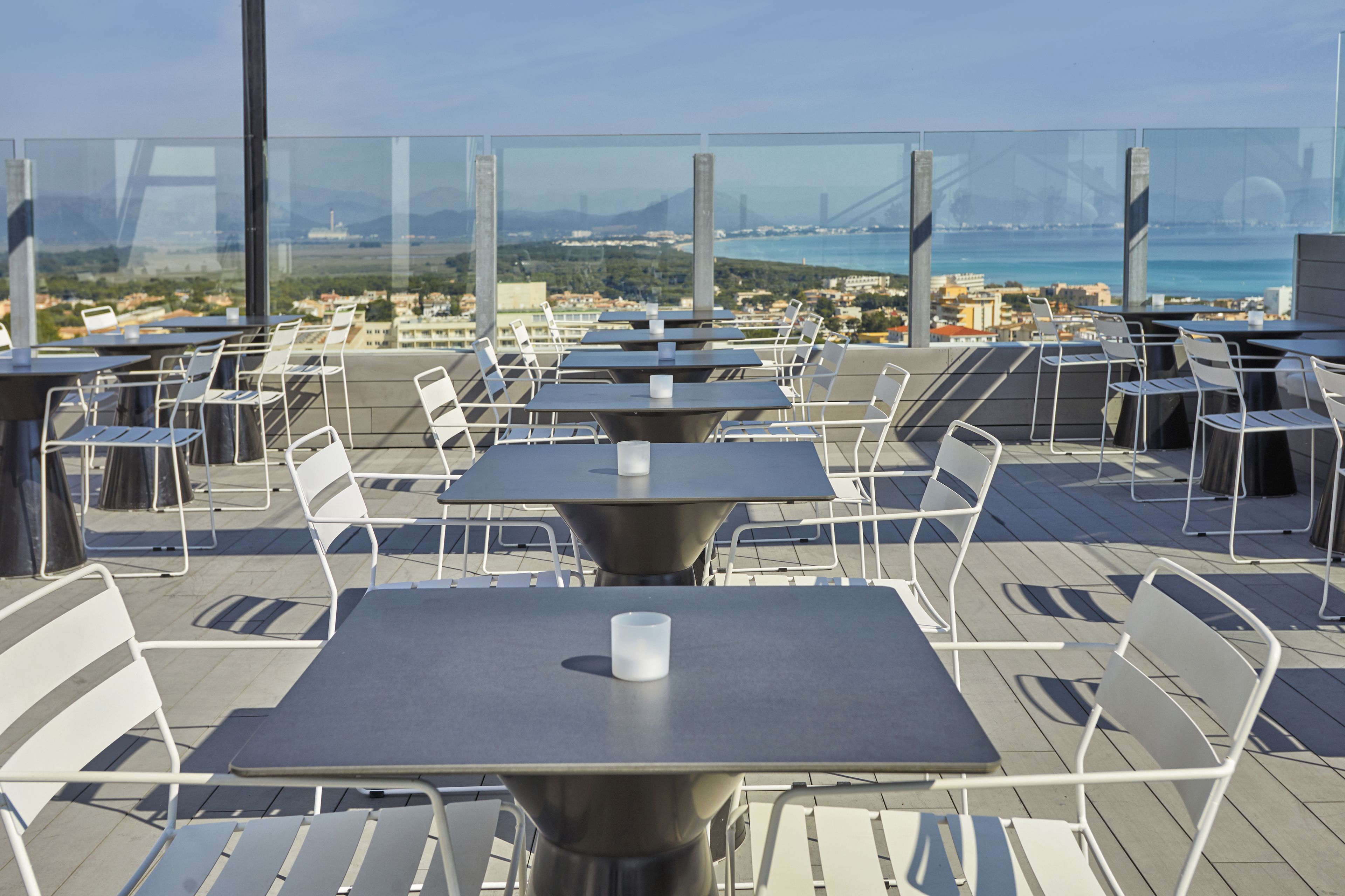 Un restaurante en la azotea con mesas y sillas, que ofrece vistas a la ciudad y un puente.