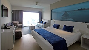 Habitación de hotel con una cama grande, un escritorio, una silla, un sofá y un cuadro de un muelle.