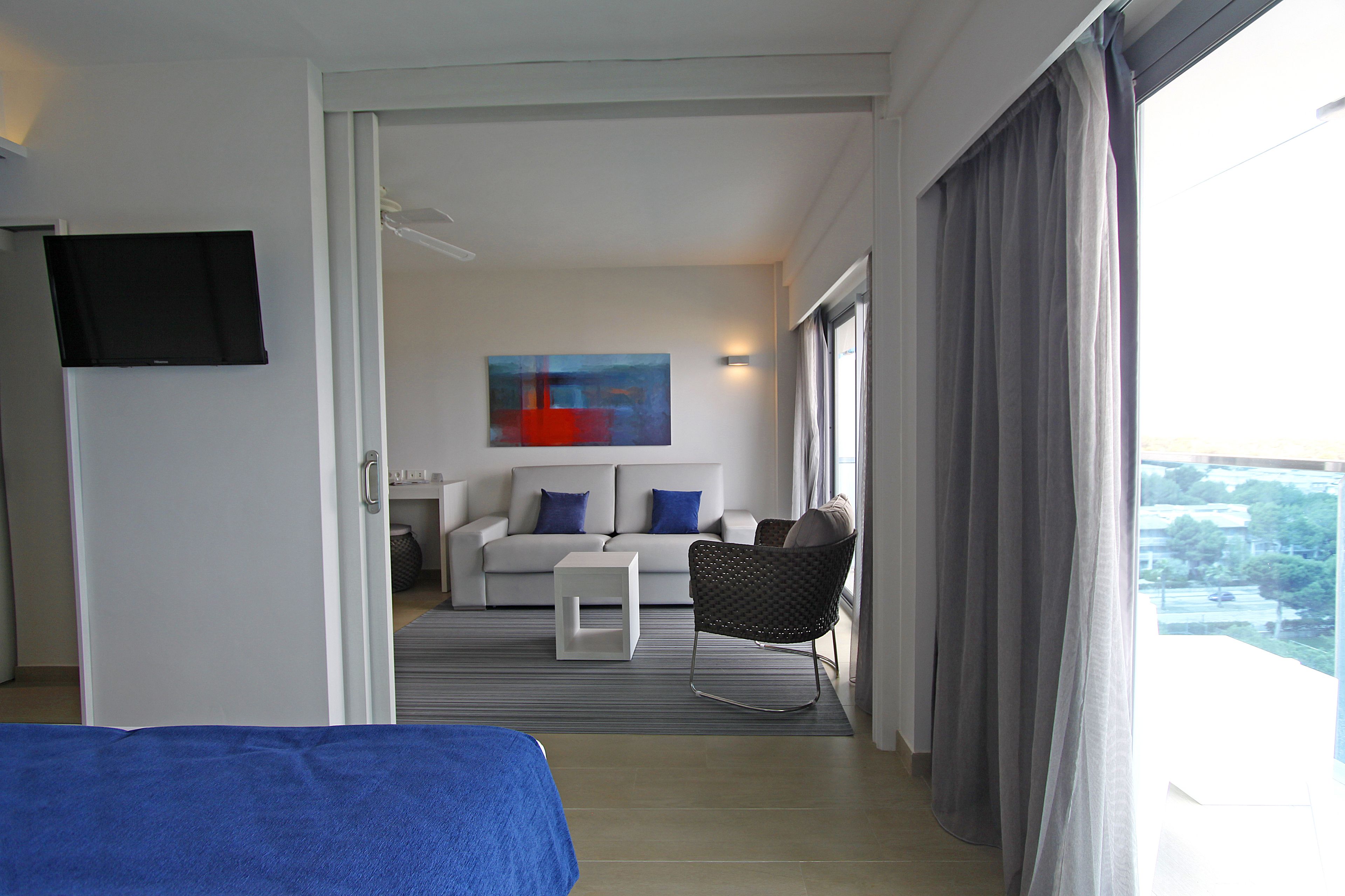 A hotel room with a bed, a sofa, a small table, a chair, and a painting on the wall.