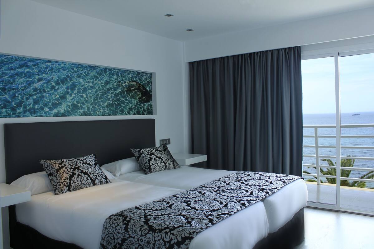 Une chambre d’hôtel moderne avec un grand lit, une vue sur la mer depuis un balcon et un tableau accroché au mur.